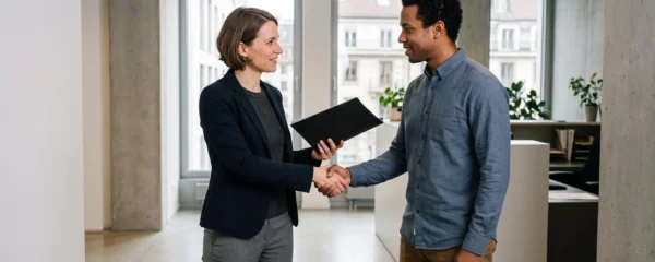 HR compliance specialist welcoming a new employee with a handshake in a bright Swiss office.